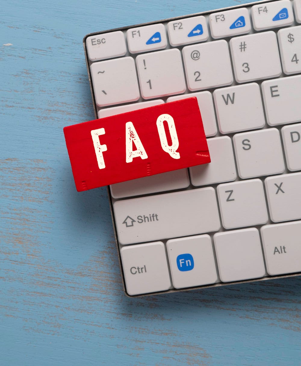 A red wooden block marked FAQ resting on a white computer keyboard